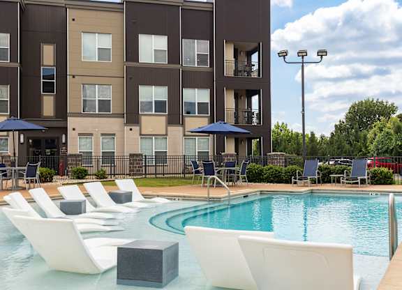 A large swimming pool with lounge chairs and umbrellas in front of a multi-story apartment building. at Alinea Town and Country Luxury Apartments in Des Peres MO 63131.