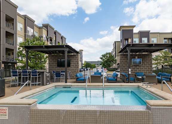 A pool area with a hot tub and lounge chairs in front of apartment buildings at Alinea Town and Country Luxury Apartments in Des Peres MO 63131..
