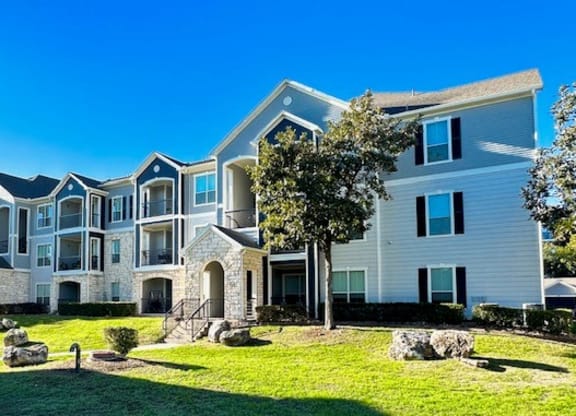 an apartment building with grass and trees in front of it