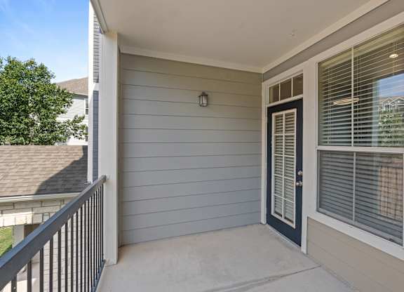 A small balcony with a black door and a window with blinds.