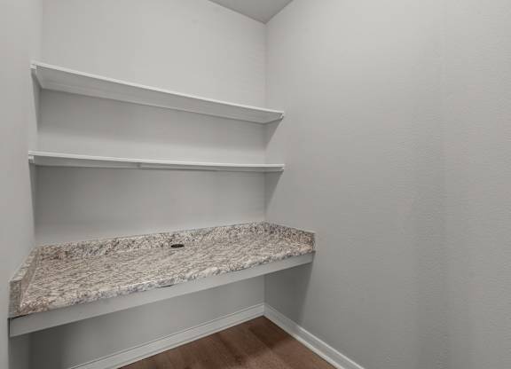 A corner of a room with a granite countertop and shelves.