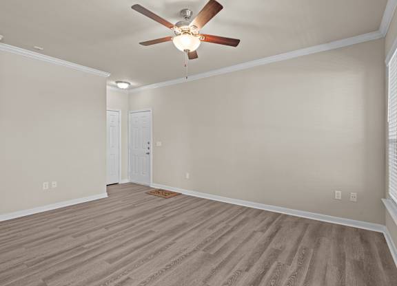 A room with a ceiling fan and light fixture, wooden flooring, and a door.
