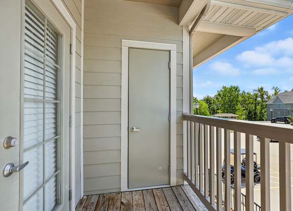A white door is on the left of a balcony with a wooden floor at Bramblett Hills Luxury Apartments in O Fallon MO 63366