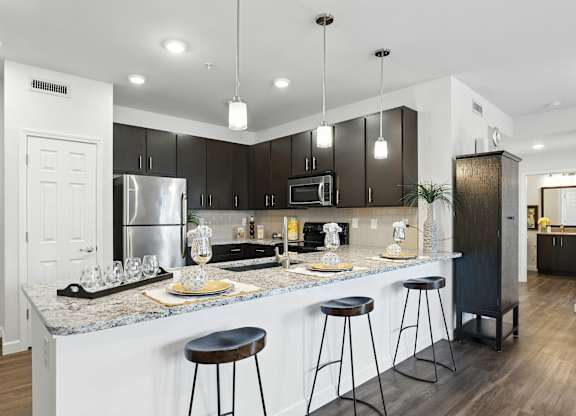 A modern kitchen with a bar area and stools at Bramblett Hills Luxury Apartments in O Fallon MO 63366