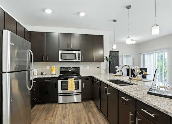 A modern kitchen with a stainless steel refrigerator and black cabinets  at Bramblett Hills Luxury Apartments in O Fallon MO 63366