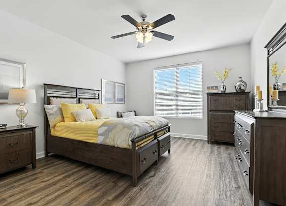A bedroom with a bed, dresser, and nightstand at Bramblett Hills Luxury Apartments in O Fallon MO 63366