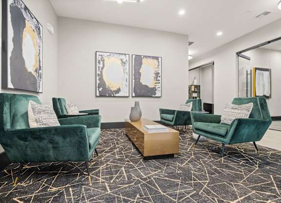 A living room with green velvet chairs and abstract art on the wall.