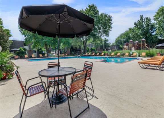 a table with chairs and an umbrella next to a pool
