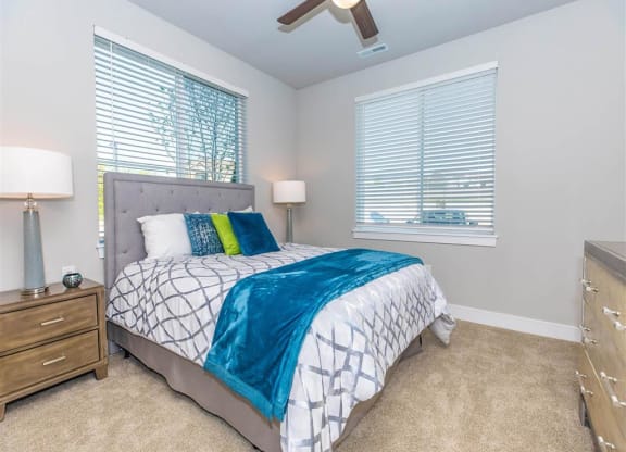 a bedroom with a bed and a ceiling fan and two windows