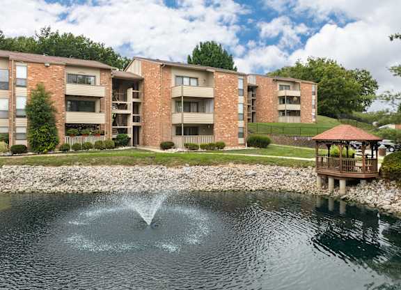 A fountain in the middle of a pond in front of apartment buildings.