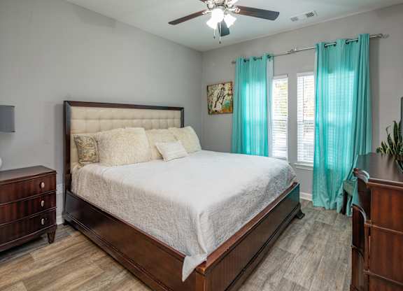 A bedroom with a large bed, a ceiling fan, and a dresser.