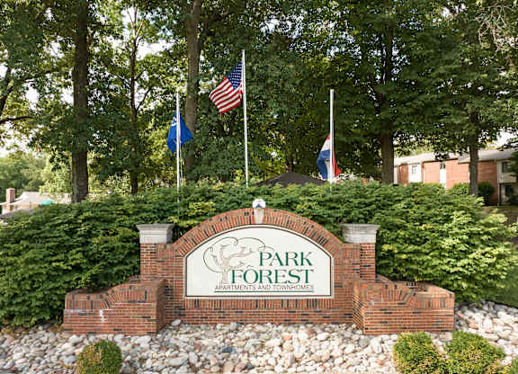 A sign for Park Forest Apartments and Townhomes is surrounded by trees and flags.