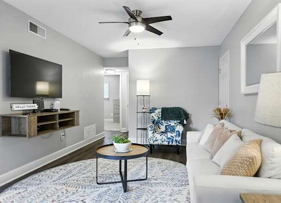A living room with a white couch, a round table, and a flat screen TV mounted on the wall.