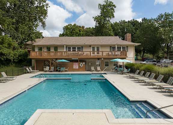 A large swimming pool in front of a house with a pool house.