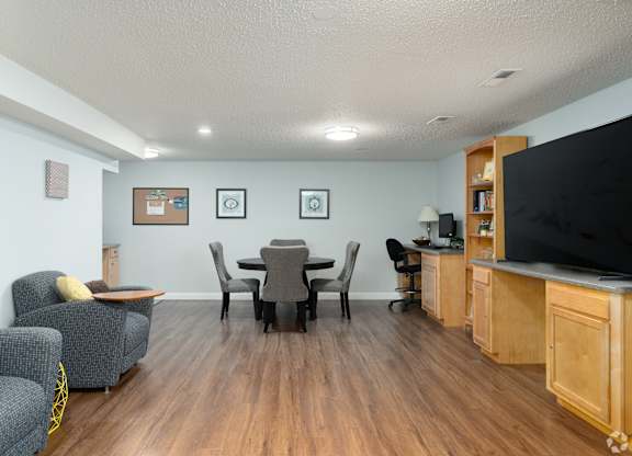 A living room with a grey couch, a black chair, a wooden cabinet, and a television.