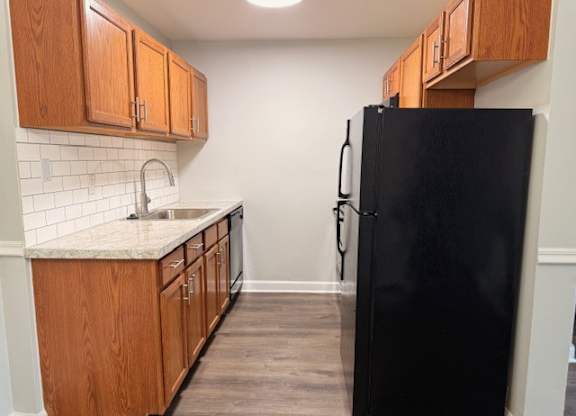 A black refrigerator stands in a kitchen with wooden cabinets.