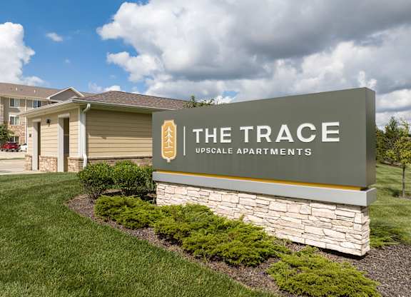 A sign for The Trace Upscale Apartments in front of a building.