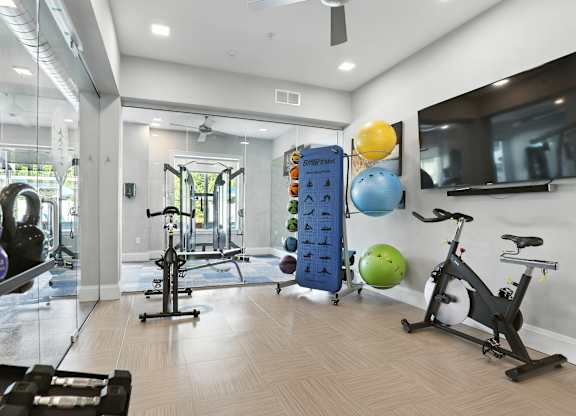 A gym with a variety of equipment including a stationary bike, a treadmill, and a rowing machine.
