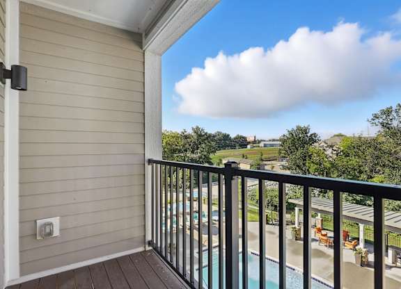 A balcony with a pool and trees in the distance.