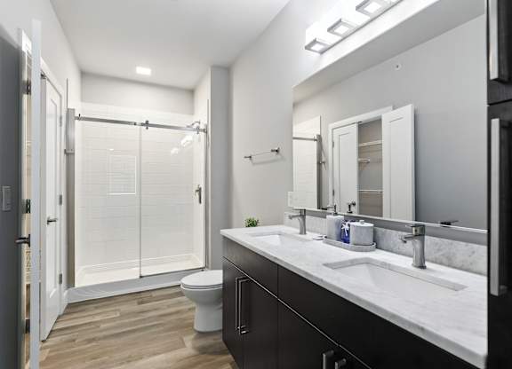 A bathroom with a toilet, sink, mirror, and shower.