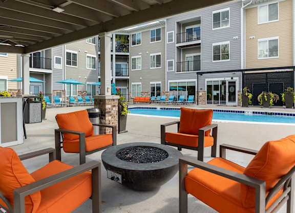 A patio with orange chairs and a fire pit.