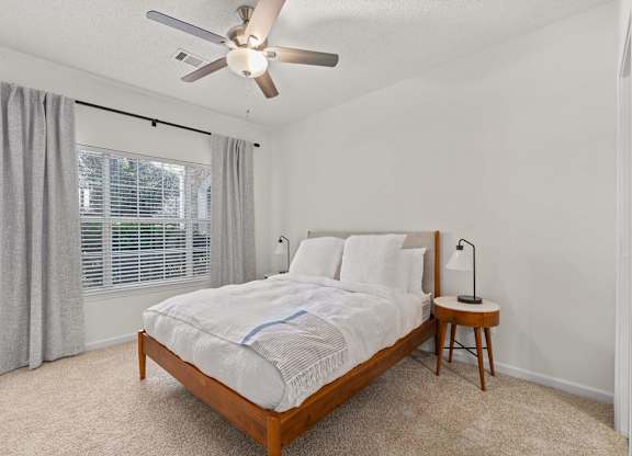 A bedroom with a bed, a small table, and a ceiling fan.