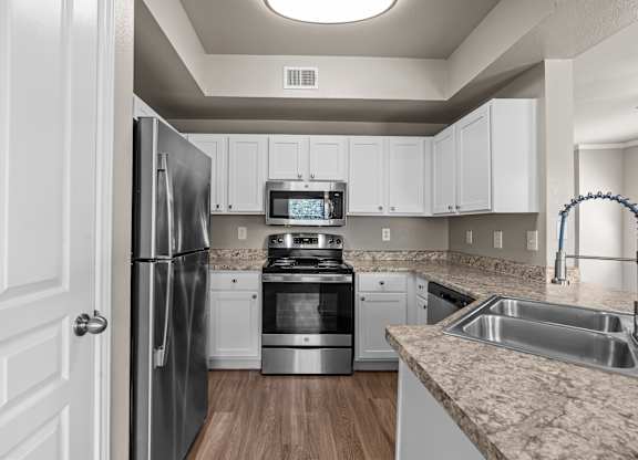 A kitchen with a refrigerator, oven, sink, and microwave.