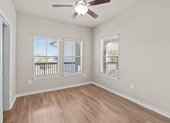 A room with a ceiling fan and two windows with blinds.
