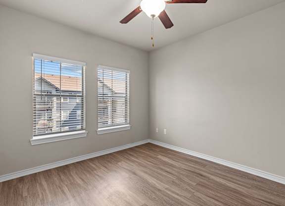 A room with a ceiling fan and two windows.