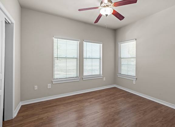 A room with a ceiling fan and two windows.