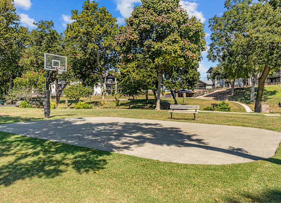A basketball court surrounded by trees and a bench.