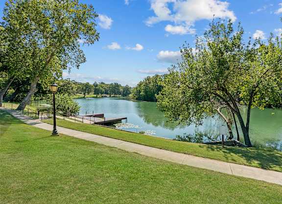 A serene park with a lake, trees, and a clear sky.