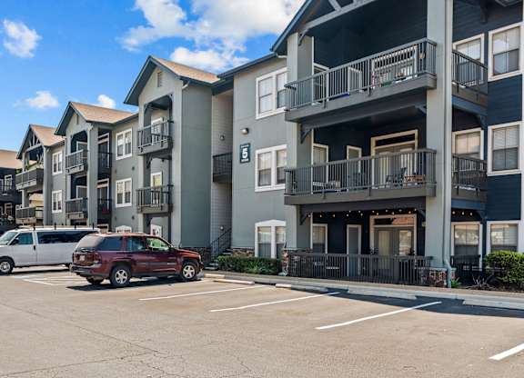 A row of apartment buildings with cars parked in front.