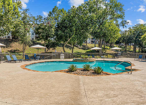 A sparkling pool surrounded by trees and chairs.