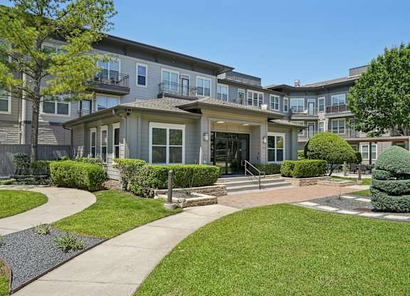 Clubhouse entrance with manicured landscaping and tiered shrubs at Highline Urban Lofts Apartments, Texas, 77429
