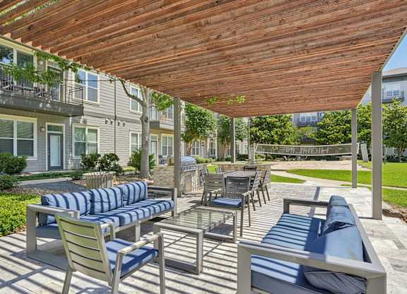Covered outdoor lounge with striped seating and grilling station at Highline Urban Lofts Apartments, Cypress, TX