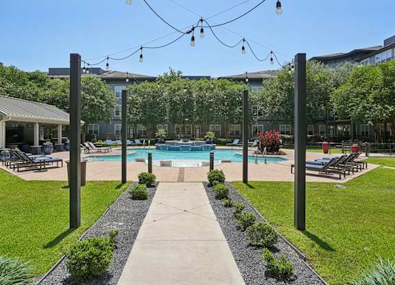 Resort style pool with lounge chairs and string lighting at Highline Urban Lofts Apartments, Cypress, TX 77429