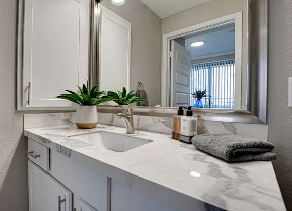 Bathroom vanity with marble countertop and mirror at Carmel Creekside Apartments, Fort Worth, TX 76137
