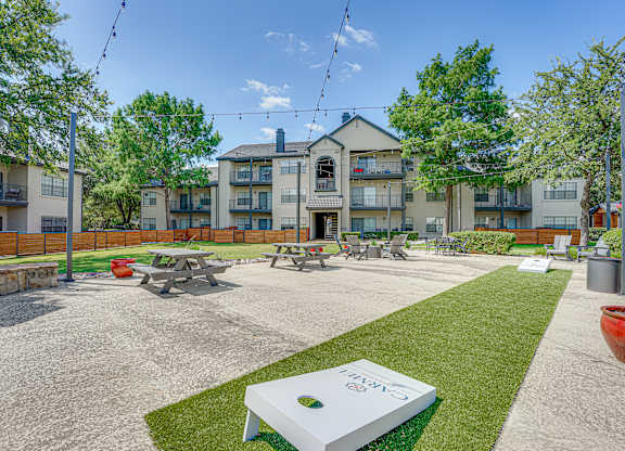 Outdoor courtyard with picnic tables and cornhole game at Carmel Creekside Apartments, Fort Worth, TX 76137