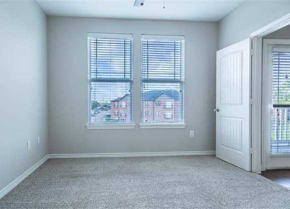 A room with a carpeted floor and a view of a house through the window.