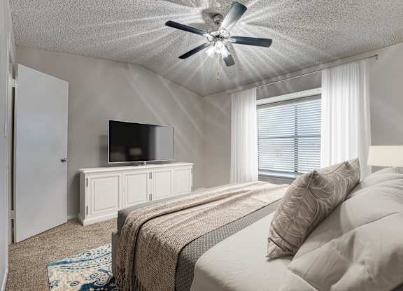 A bedroom with a bed, a television, and a ceiling fan at Indian Creek Apartments, Carrollton, TX