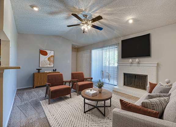 A living room with a fireplace, a television, and a ceiling fan at Indian Creek Apartments, Carrollton, TX, 75007