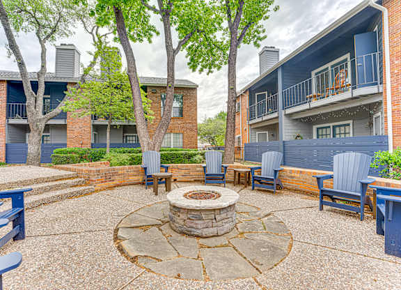 A courtyard with a fire pit surrounded by chairs and trees.