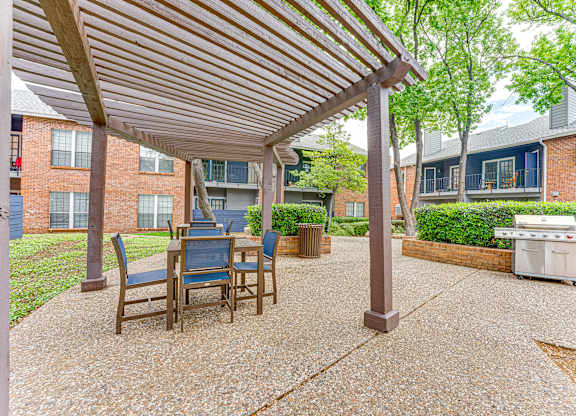 A patio with a table and chairs under a wooden roof.