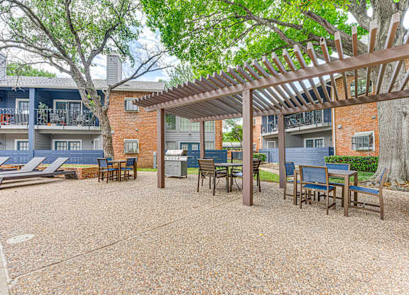 A patio with a pergola and chairs is surrounded by apartment buildings.