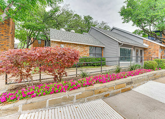 A house with a grey roof and a brick wall with a flower bed in front.