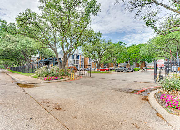 A tree-lined street with a sidewalk and a fence.