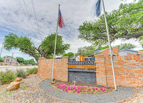 The entrance to a property named Manhattan with a brick wall and a sign.