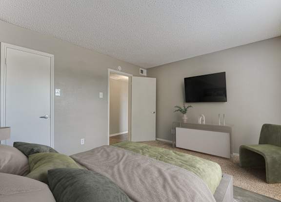 A bedroom with a bed, a chair, and a TV on the wall.