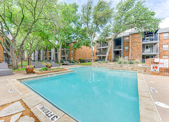 A swimming pool surrounded by trees and apartment buildings.